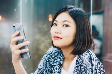 Asyalı genç kadın kahve dükkanı ahşap masa içinde otururken cep telefonu kullanmak