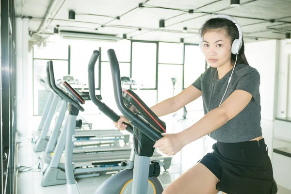 Fitness women cycling on bike and listening music in fitness gym