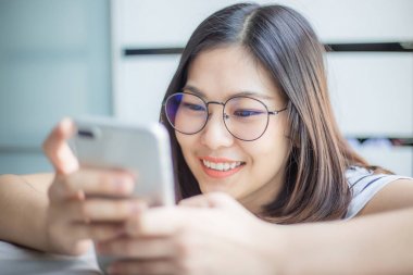 Mutlu genç Asyalı kadınlar Smartphone rahat yatak manifatura iletilerde kullanma