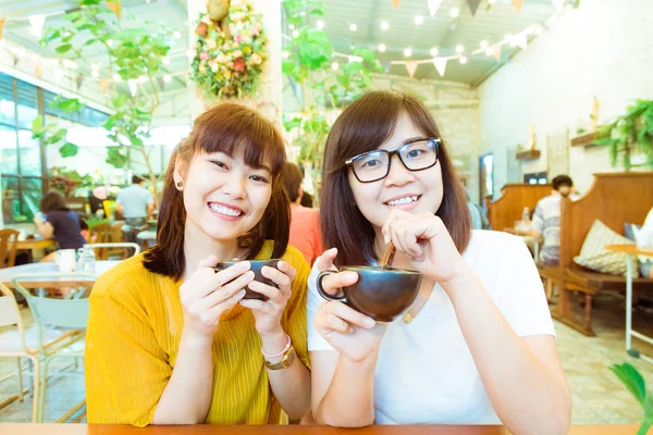 Beber con la amiga de dos mujeres sonrientes riendo mientras chismorrean —  Fotos de Stock