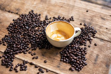 Beyaz fincanda kahve, tahtanın üstünde kavrulmuş kahve çekirdeği.