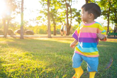 Mutlu çocuk parkta yürüyor yaz günbatımında çimenlerde oynuyor.