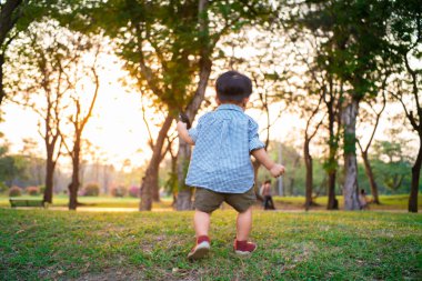 Küçük Asyalı çocuk parkın gün batımında yeşil çimlerde yürümeyi dene, Parktaki bebek çocuk