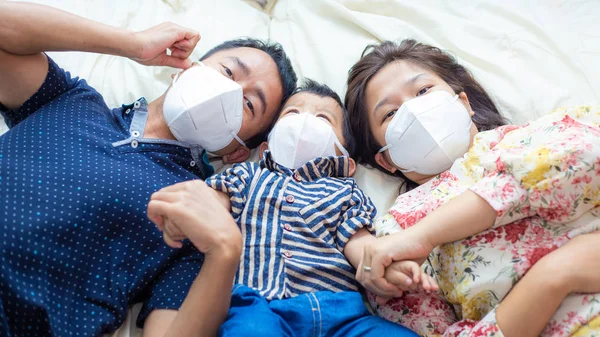 Asian family wearing protective visus Covid 19 and pm 2.5 N95 mask lying on white blanket healthy concept