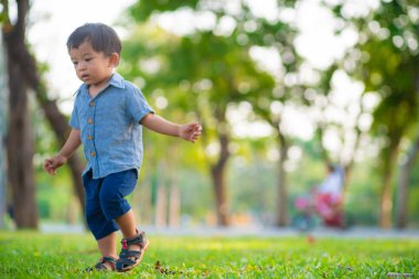 Sevimli çocuk yeşil çimlerde yürüyor şehir parkında gün batımında mutlu çocuk