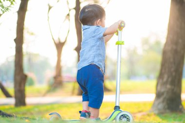 Küçük çocuk şehir parkında gün batımında çocuk scooter 'ı oynuyor.
