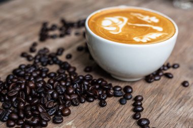 Ahşap masa üzerinde fasulye desenli Latte sanat kahvesi, sıcak içecek.