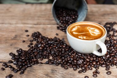 Ahşap masa üzerinde fasulye desenli Latte sanat kahvesi, sıcak içecek.