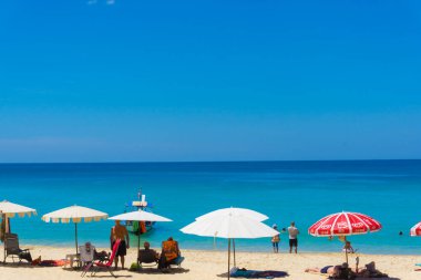 Beyaz kum plajı üzerinde şemsiyesi olan renkli plaj sandalyesi.