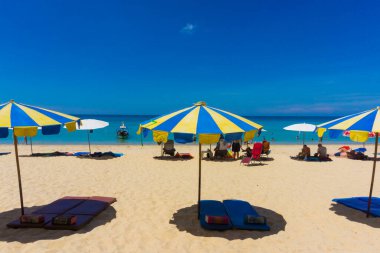 Beyaz kum plajı üzerinde şemsiyesi olan renkli plaj sandalyesi.