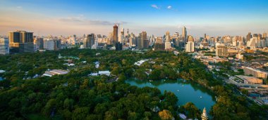 Bangkok şehir merkezindeki modern ofis binaları ve apartmanların çevresindeki Lumpini parkı manzarası. Tayland, Bangkok 'ta günbatımı gökyüzü bulutları var..