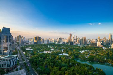 Bangkok şehir merkezindeki modern ofis binaları ve apartmanların çevresindeki Lumpini parkı manzarası. Tayland, Bangkok 'ta günbatımı gökyüzü bulutları var..