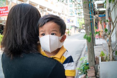 Asyalı sevimli çocuk ve anne N95 maskeli açık şehir binası Coronavirus 'u ve hava kirliliği pm2.5' i koruyor. Bilinç virüsü konsepti yaydı