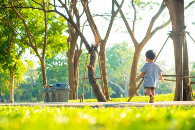 Yeşil çimlerde yürüyen sevimli Asyalı çocuk yaz tatilinde gün batımı ışığı...