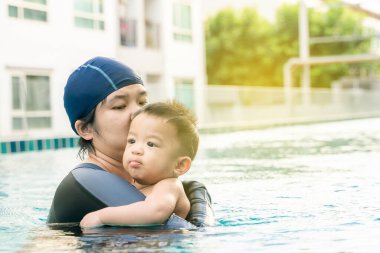 Anne, bebeğe 9 aylık havuzda yüzme, anne ve oğul öğretiyor.