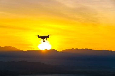 Dron kuadkopteri, gün batımı siluetinde uçuyor. Doğa manzarası.