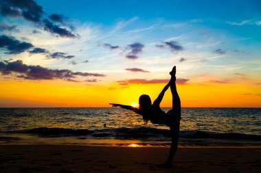 Sahilde gün batımı renkli gökyüzünde sağlıklı kadınların silueti yogası.