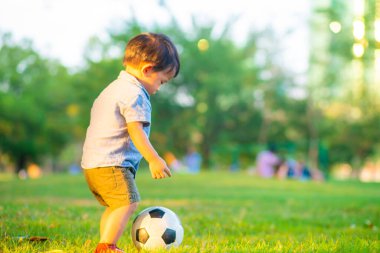 Yeşil çimlerde futbol oynayan sevimli küçük çocuk ilk kez gün batımında oynuyor.
