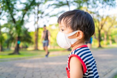 Korunaklı bir n95 maske takan Asyalı çocuk yeşil parkta, Coronavirus 'ta ve hava kirliliği kavramında yürüyor..