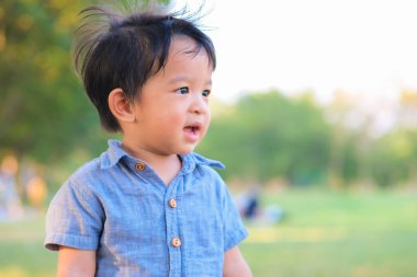 Şehir parkında yeşil çimlerin üzerinde duran mavi tişörtlü küçük mutlu çocuk gülümseyen bebek çocuk.