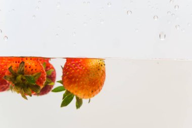 Suda taze çilek meyvesi, beyaz arka planda izole edilmiş.