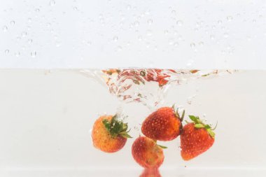 Suda taze çilek meyvesi, beyaz arka planda izole edilmiş.