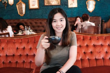 Asyalı kadınlar ellerinde siyah bardakla klasik kafede sıcak latte içerler.