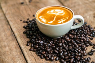 Ahşap zemin üzerinde kahve çekirdeği olan Latte art kahve fincanı, iş içme konsepti