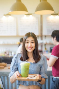 Mutlu gülümseyen Asyalı kadınlar buz eşliğinde yeşil çay içerler.