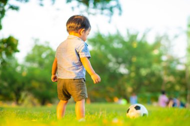 Yeşil çimlerde futbol oynayan sevimli küçük çocuk ilk kez gün batımında oynuyor.