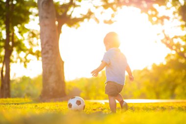 Yeşil çimlerde futbol oynayan sevimli küçük çocuk ilk kez gün batımında oynuyor.