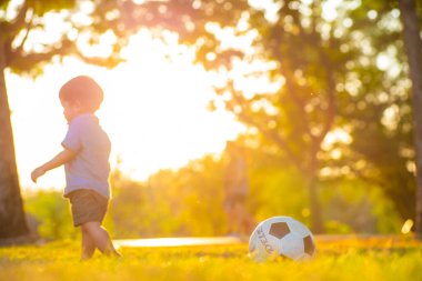Yeşil çimlerde futbol oynayan sevimli küçük çocuk ilk kez gün batımında oynuyor.
