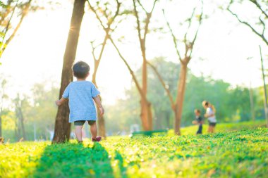 Sevimli mutlu çocuk yeşil çimlerde oynuyor günbatımında ışıklı şehir parkında, parkta küçük çocuk