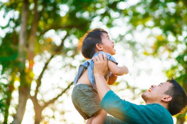 Mutlu bir babanın portresi, küçük oğlunun elini tutuyor. Şehir parkında gün batımında taşınıyor. Babasıyla dışarıda oynayan tatlı çocuk..