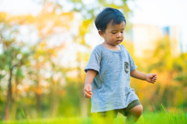Sevimli mutlu çocuk yeşil çimlerde oynuyor günbatımında ışıklı şehir parkında, parkta küçük çocuk