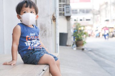 Küçük çocuk beyaz maske takıyor. PM2.5 ve CVid 19 'u koruyor. Kafede oturuyor, sağlıklı bir konsept.