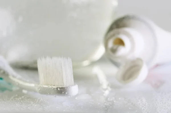 Tandenborstel, tandpasta en een glas water op een natte tafel sluiten — Stockfoto