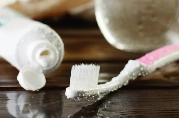 Natte roze tandenborstel en open buis van tandpasta op een houten tabl — Stockfoto