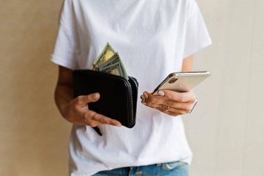 Cüzdan ve cep telefonu kadınların elinde, nakit ödeme ya da alışveriş konsepti. Kız, siyah deri çantadan parayı çıkar, el çantasına 100 dolar koy..