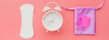 Poşetli regl kupası, hijyenik ped, pembe arka planda çalar saat. O dönemde alternatif kadın hijyen ürünü. Kadın sağlığı kavramı. 