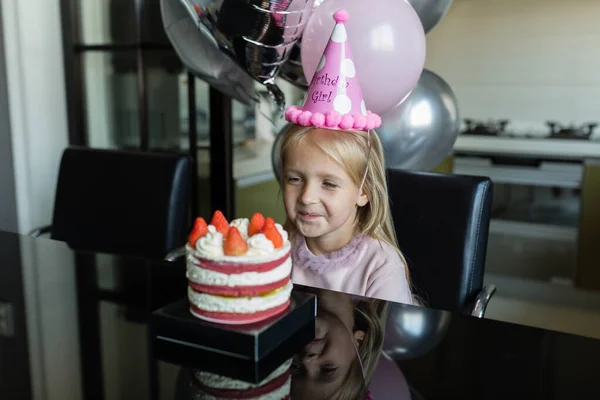 Indoor shot de niña bastante alegre con el pelo rubio soplando la vela, celebrar 6 años de edad cumpleaños, usar vestido de moda, tienen expresiones emocionadas. Concepto de infancia feliz — Foto de Stock