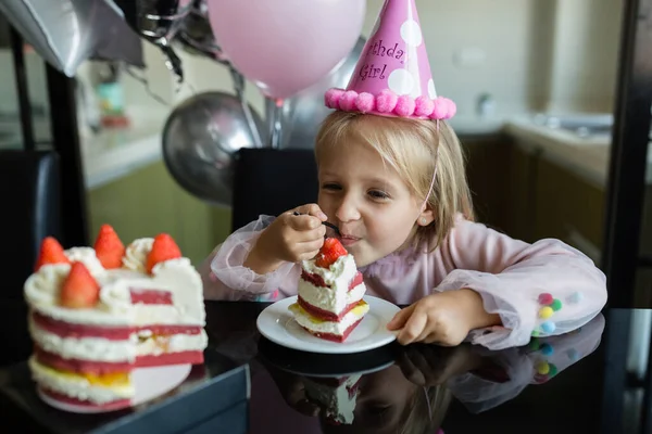 Vnitřní záběr pěkné radostné holčičky s blond vlasy sfouknutí svíčky, oslavit 6 let staré narozeniny, nosit módní šaty, mají vzrušené výrazy. Šťastné dětství koncept — Stock fotografie