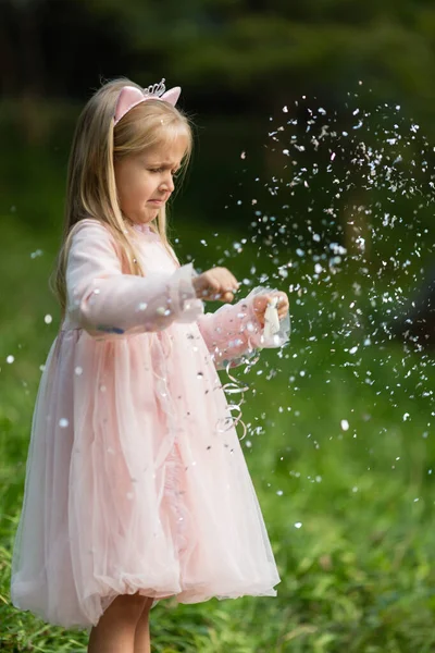Niña con estilo con el pelo rubio lanzando confeti en el parque. Cumpleaños celebración al aire libre, diversión niño ocio — Foto de Stock