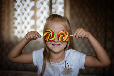Şekerli lolipopu olan komik çocuk, mutlu sarışın kızın evde renkli şeker lolipop yerken çekilmiş fotoğrafı.