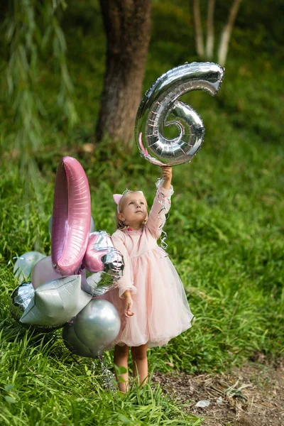 Szabadtéri lövés elég vidám kislány szőke haj ünnepli 6 éves születésnapját lufikkal, viselni divatos ruhát, van izgatott kifejezések. Boldog gyermekkori emlékeket — Stock Fotó