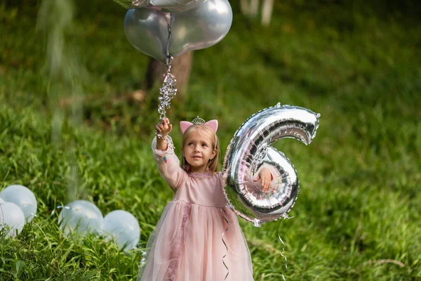 Outdoor shot van mooie vrolijke kleine meisje met blond haar vieren 6 jaar oude verjaardag met ballonnen, dragen modieuze jurk, hebben opgewonden uitdrukkingen. Gelukkige jeugdherinneringen — Stockfoto