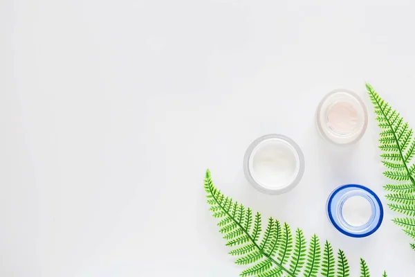 Flat lay with Natural organic cosmetics: cream on white background with green leaves. Skincare, cosmetology, dermatology concept. Beauty certificate, blog style. Top view, mockup, overhead