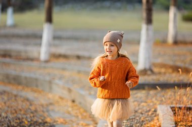 Sonbahar parkında ginkgo ağaçlarıyla yürüyen şirin, şık küçük bir kız. Sonbahar çocukları moda. Mutlu bir çocukluk. Yaşam tarzı portresi