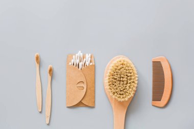 Doğal banyo aksesuarları: ahşap tarak, bambu diş fırçası, masaj fırçası, gri kağıt arka planda kulak çubukları. Sıfır atık. Model, düz yatak, şablon, üst görünüm, genel giderler