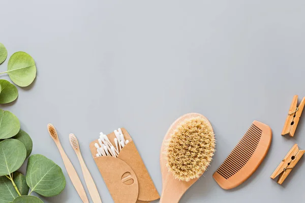 Doğal banyo aksesuarları: ahşap tarak, bambu diş fırçası, masaj fırçası, gri kağıt arka planda kulak çubukları. Sıfır atık. Model, düz yatak, şablon, üst görünüm, genel giderler